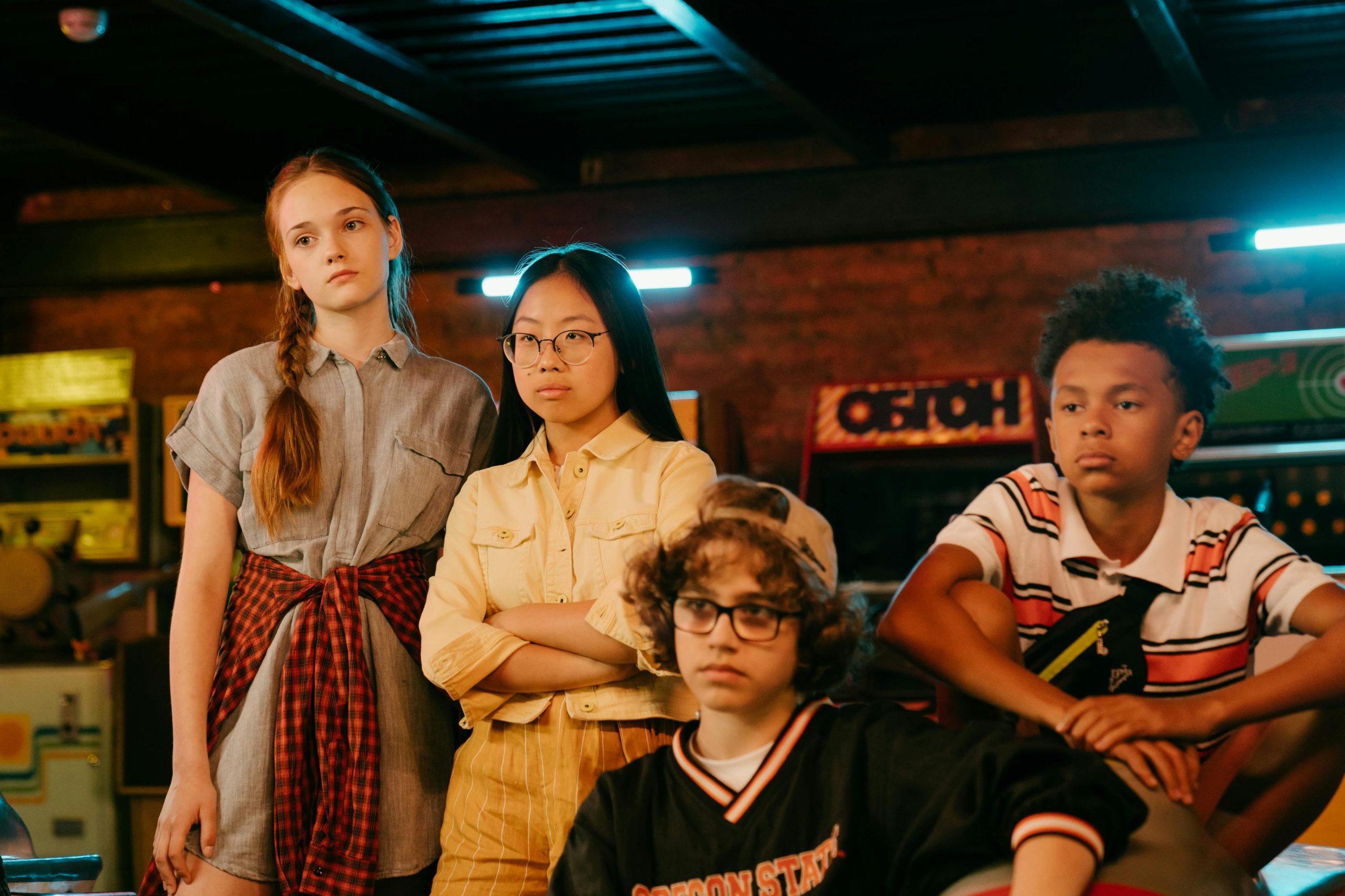 Group of diverse teenagers posing in a retro arcade with neon lights and vintage style.